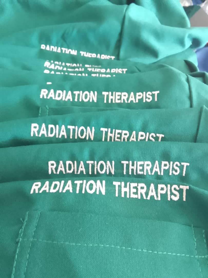 Stack of green work garments branded with the words Radiation Therapist.