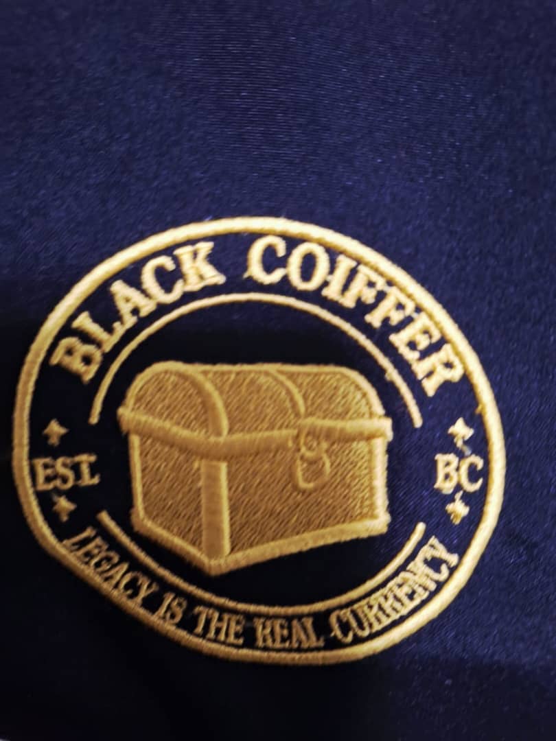 Close-up of a circular dark-and-gold embroidered badge with a coffin motif.