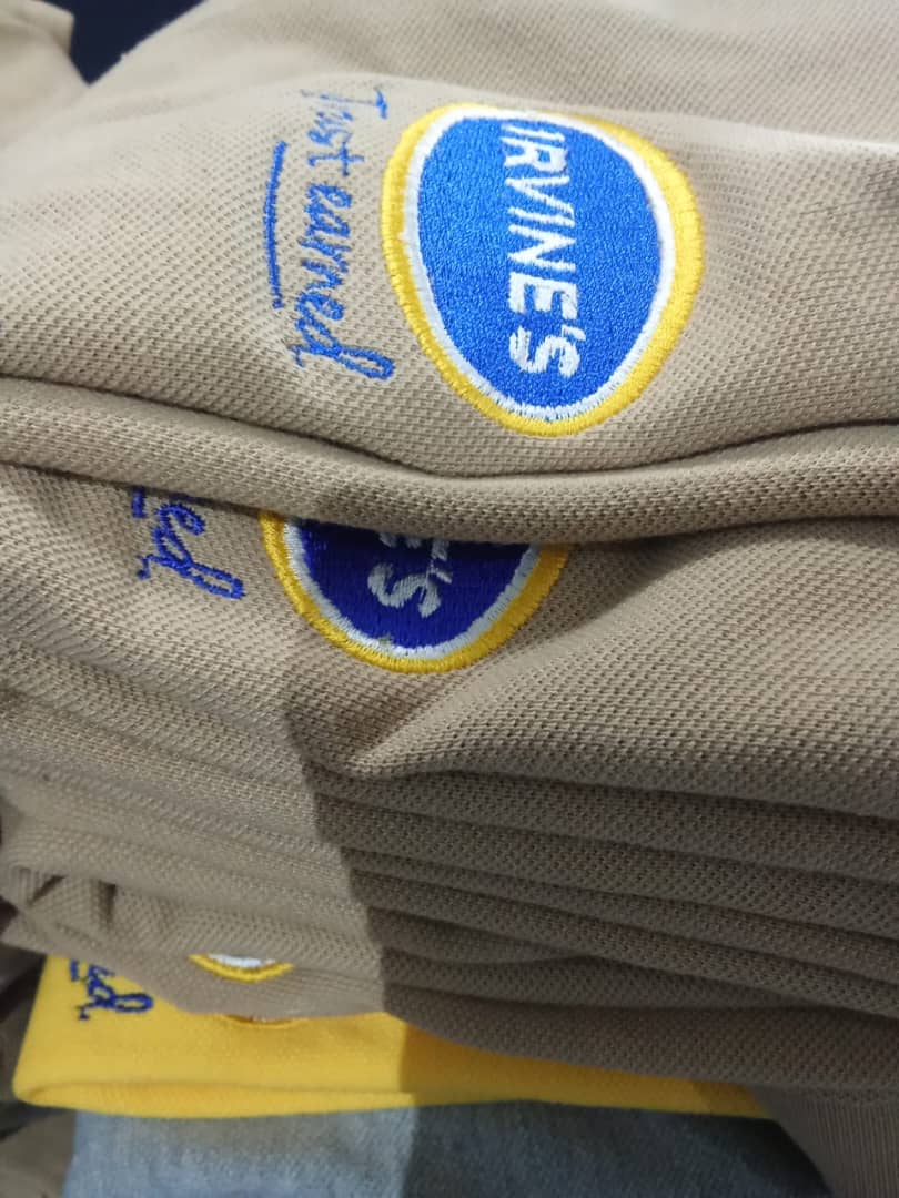 Stack of grey polo shirts embroidered with blue and yellow Irvines branding.